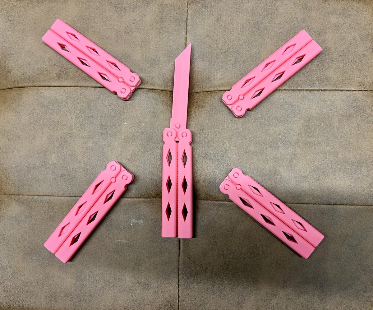 Five pink butterfly knife trainer fidgets, blunt practice knives, arranged in a star pattern