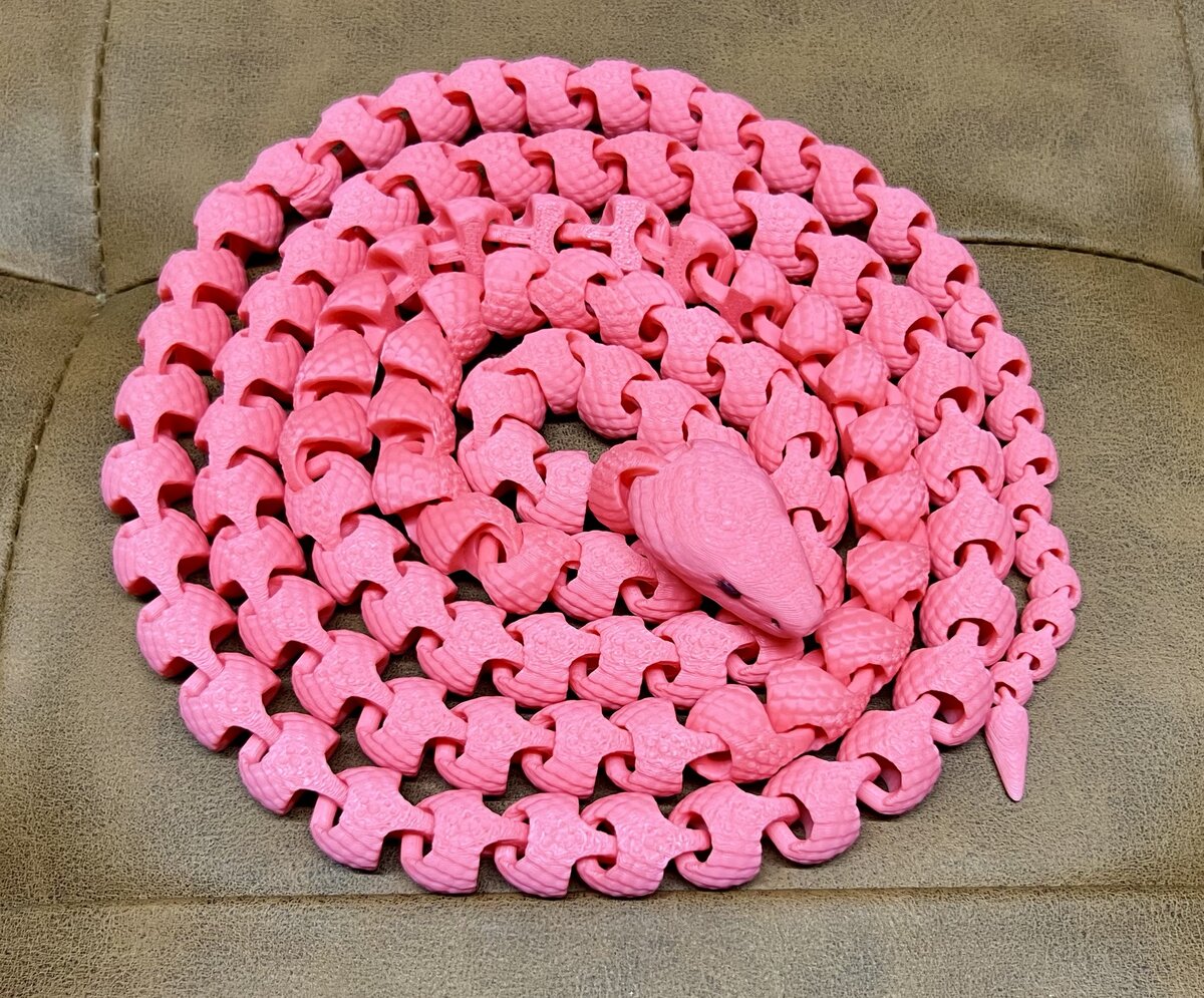 Pink chain-link snake with a sculpted head and eyes, coiled on a couch